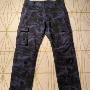 Vogue Camo Cargo Byxor - Sjukt coola cargo byxor med camo print på, byxorna har flera stora fickor med knapp på sidan och bak på byxan. Priset går att diskuteras och kan skicka fler bilder om det önskas.