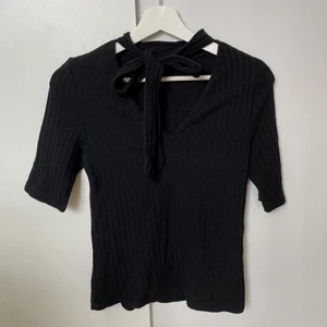 Topp med knytning i halsen - Fin svart topp med v-ringning och knytning. Passar till det mesta, använd en del men i bra skick.