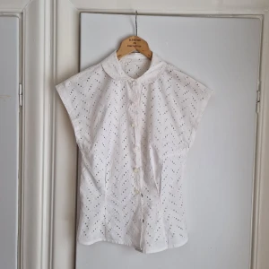 Nätt, vit Vintageblus  - Urgullig vintageblus med spännande "håligt" tyg. Figursygg. Tryckknappar med påsyda vita knappar utanpå.  Vintage, troligtvis 40-tal eller 50-tal.  Perfekt till våren och sommaren med ett linne eller bara bh under. Fint skick, behöver tvätt, lite gulnad.