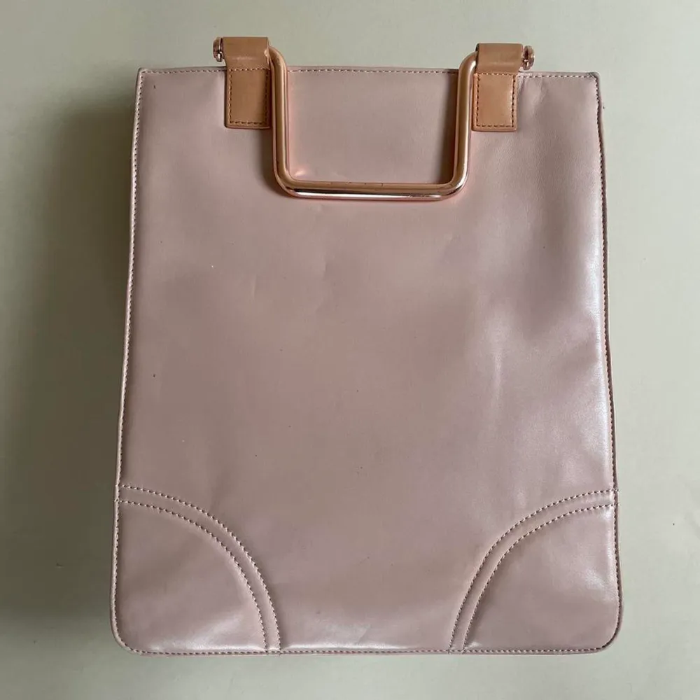 -Pink Leather -Blue Lining -Metallic Hardware with Embossed Branding -Comes with Leather Shoulder Strap and Metal Handles for Versatile Wear -Snap Closure -2 Bag Compartments that can hold MacBook -2 phone pockets -2zip pockets  Shows some signs of wear. Väskor.