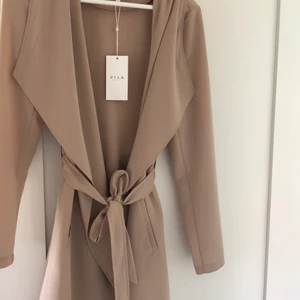 Beige vårkappa  - Säljer min vårkappa som aldrig är använd, prislappen på finns kvar. Kappan är gjort i ett tunnt material perfekt nu till våren och sommaren, den är köpt på vila💕