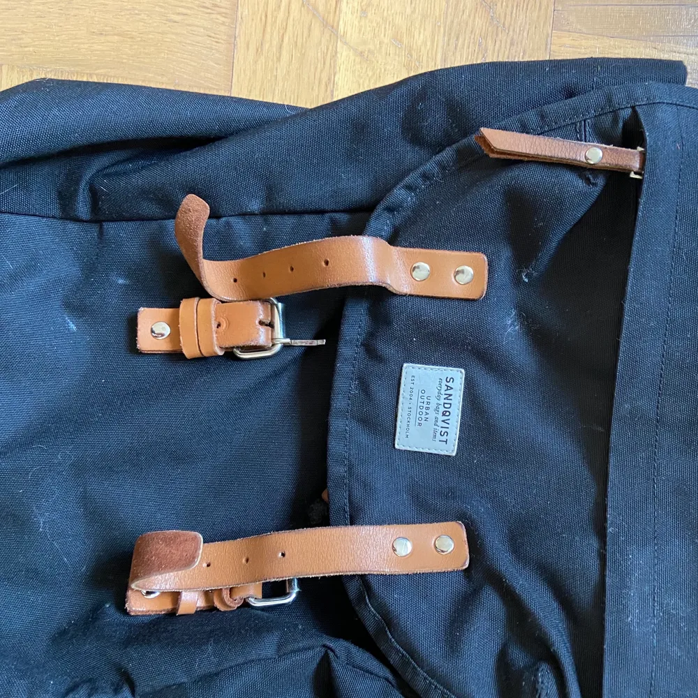 En rymlig svart ryggsäck med bruna ödet detaljer, använd under flera års tid. Den är helt och ren förutom att den ena spännet har lossnat på framsidan. Men den fungerar ändå för du sluter igen väskan med bandet. Väskor.