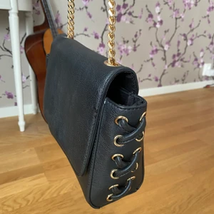 Handväska - Svart axelremsväska från New Look! Detaljer på sidorna, guldig kedja och litet innerfack! Köpt för några år sedan för ca 250kr! Köpare står för frakt!