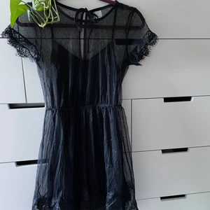 Svart spetsklänning 32 - Liten svart spetsklänning från H&M. Spetsdetaljer på ärmar och nertill på kjolen. Svart underklänning. Mått mätt liggande platt. Längd hela klänningen: 83 cm. Längd kjol: 47 cm. Byst: 40 cm. Midja 31 cm. (ta mått gånger två på byst och midja)