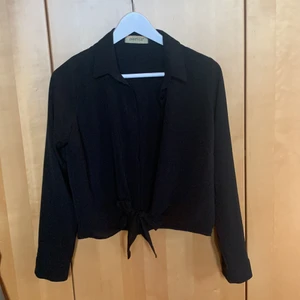 Skjorta med knyte  - Svart skjorta med knappar framtill, längst ned finns det möjlighet att knyta för en extra detalj på skjortan, går även att stoppa in om man inte vill. Aldrig använd