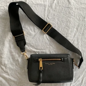 Axelremsväska från Marc Jacobs - Säljer en axelremsväska från Marc Jacobs. Svart med guldiga deltajer. Skinn. Axelremmen på bilden är från Lindex med ordinarie axelrem i skinn följer med! Väskan är i gott skick men har små slitningar på dragkedjan.