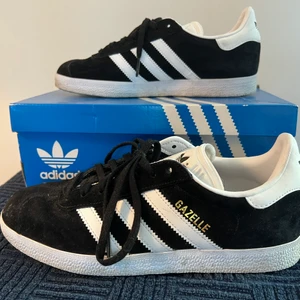 Adidas GAZELLE skor strl. 38 svarta - Ett par skor från Adidas namn GAZELLE i strl. 38 använda fåtal gånger lite smutsiga och lite damm på men går lätt att få bort. Nästan som nya. Mycket bra skick. Skolåda fås med. Köparen betalar frakten. 