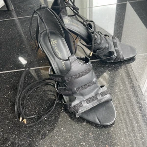 Svarta sandaletter med snörning - Svarta sandaletter med snörning md gulddetalj. 9cm hög och väldigt bekväm klack. Endast använda en gång! Läder invändigt.