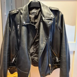 Zara skinnjacka - Supersnygg skinnjacka från Zara. Köptes i augusti för 750kr. Använd ca 5-7ggr då den var lite liten så i väldigt fint skick, så gott som ny. Hängöglan är trasig (se bild 3) men går lätt att sy. Storlek L, men mer en S om man inte vill ha den tajt.