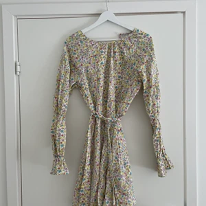 Blommig klänning  - Blommig klänning med öppen rygg och band att knyta i midjan, i storlek 36.