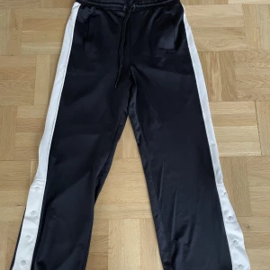 Sköna brallor - Svarta byxor från H&M med vit linje på sidbenet. De har dragsko och två fickor. De har även knappar i slitsen. Innerbens sömmen är 73cm. Aldrig använda, helt nytt skick