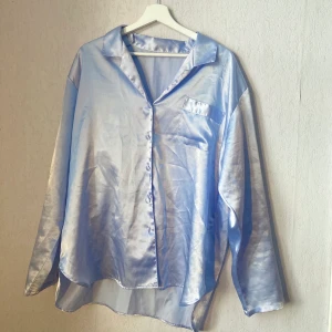 Pyjamas  - Pyjamas i satin material. Ljusblå, glansig. Skön och bekväm passform. Skjortan är en del av ett set (byxor i separat annons).  Okänt märke. Aldrig använd av mig och plagget är i mycket gott skick.   Paketpris set= 250