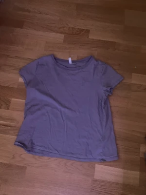 En tröja. - En lila T-shirt som har ett litet hjärta på sig uppe i hörnet.