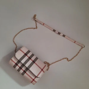Axelremsväska - En lookalike, alltså inte äkta Burberry. Materialet känns som vinyl. Kedjan går att ta av. Storlek ca 20x13cm. Kan hämtas i Stockholm.