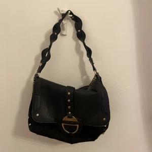 Väska  - Säljer denna svarta väska med guldiga nitdetaljer då den inte kommer till användning. Har haft denna länge men den är i bra skick, den har ngn liten skinn skada men inte mer. Den är väldigt rymlig o är helt svart på andra sidan o har ett längre band även
