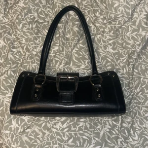 Y2K Väska - Svart axelväska med stort silverspänne från tidigt 2000-tal!🪩 Den har bara används på 2-3 utgångar så är i väldigt bra skick. Inga synliga skador eller fläckar och dragkedja funkar som den ska. 💘 Nypris ca 400kr! 