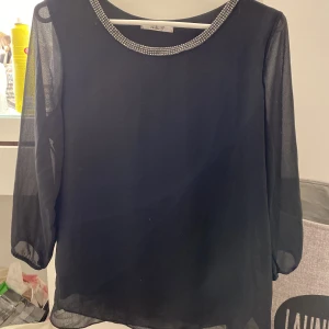 Svart blus rhinestone - Svart söt blus med halvlånga ärmar och resår i svart. Storlek S från hollys, jättefint skick. Rhinestones runt halsen. 80kr+frakt