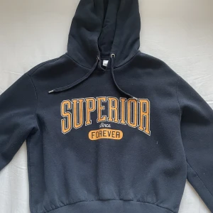 Mörkblå hoodie med tryck på - Mörkblå hoodie med text på framsidan. Lite kortare modell.