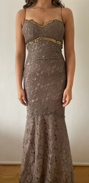 Långklänning  - Fantastiskt lång tajt brun spetsklänning som har en lättare ett band vid axlarna. Klänningen är använd enbart 1 gång men i ett superfint skick fortfarande.   Säljs pga platsbrist.