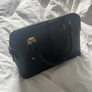 Svart Anna Fields väska  - En stor rymlig svart Anna Fields handväska i skinnimmitation med guld detaljer + 3 fack. Som ny, använt en gång. Köpt för 349kr på zalando. 