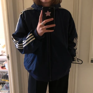 Adidas vindjacka - Marinblå Adidas vindjacka, passar mig som är en L men skulle säga att den passar s-xl beroende på vilken fit man vill ha, går även att vända på den och ha den grå också!