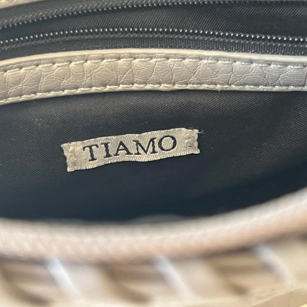 Säljer min väska från märket Tiamo, i färgen grå. I bra skick förutom att färgen på dragkedjan av väskan lossnat på vissa ställen, även mörkare baktill. . Väskor.