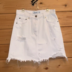 NA-KD vit jeanskjol - Vit jeanskjol från NA-KD i 100% bomull. Kjolen har aldrig använts och väntar på någon som kommer uppskatta den för vad den är. Det är en enkel vit minikjol med riven effekt och den passar med alla stilar. Fickorna är riktiga både fram och bak!