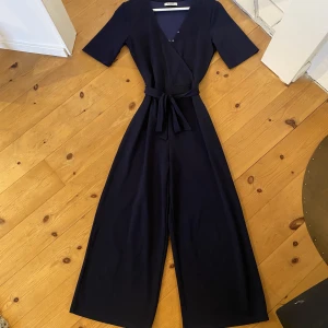 Marinblå byxdress - En jättebekväm och enkel byxdress i storlek XS. Använd ca 3 gånger. Uppsydd så den passar någon på 155cm. Även ditsydda knappar vid uringningen då jag tyckte den var för urringad, dock jättelätt att spreta bort. Nypris ca 500kr