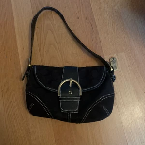 Coach handväska - Fin liten handväska, använt skick. Den har 2 fack och ett litet med dragkedja. Materialet på bandet har flagnat en del, skickar bilder vid behov. Priset ej hugget i sten. Frakt 66kr