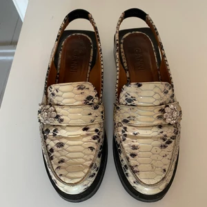 Öppna loafers från Ganni  - Underbara slingback-loafers från Ganni i storlek 39. Fyrkantig klack, ca 3 centimeter med deras numera klassiska strass-spänne. Sparsamt använda och i mycket fint skick. Väldigt tjusiga med strumpor i också. Nypris ca 3200kr. Ej sulade. 