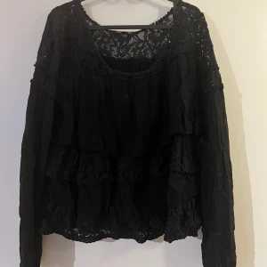 Blus - Svart blus. Volanger, varannan svart och de andra i spets. Vet inte vart den kommer ifrån 