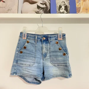Jeansshorts  - Riktigt bekväma och snygga jeansshorts i högmidjad modell med knappdetalj vid fickorna! Så söta tillsammans med en fin topp!