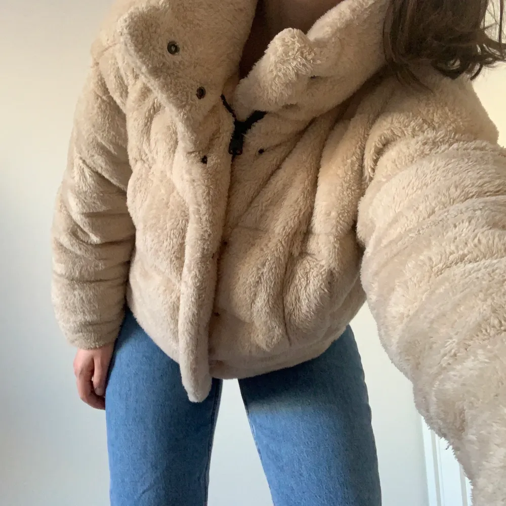 Urban outfitters beige puffer jacket. The outside is fluffy with synthetic fur-like material, very soft and cozy. The inside is lined with polyester and cotton blend. The puffer jacket is warm and a perfect spring transition piece. Fits just below the waist. There is a zipper and buttons that go up to the neck. The collar can be buttoned up to cover the neck. Has two side pockets, one of which has a hole in the lining that can be easily fixed. Size is XS, but can also fit S as it is oversized.. Jackor.