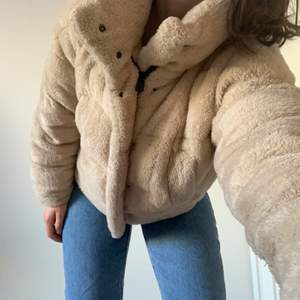 Urban outfitters beige puffer jacket. The outside is fluffy with synthetic fur-like material, very soft and cozy. The inside is lined with polyester and cotton blend. The puffer jacket is warm and a perfect spring transition piece. Fits just below the waist. There is a zipper and buttons that go up to the neck. The collar can be buttoned up to cover the neck. Has two side pockets, one of which has a hole in the lining that can be easily fixed. Size is XS, but can also fit S as it is oversized.