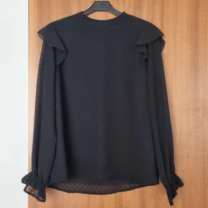 Svart spetstopp med volangdetaljer - Jättefin topp som tyvärr säljes då den inte passar längre. Använd endast två gånger, dock har lite ludd fastnat i nacklinningen och även lite framtill.