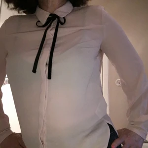 Rosa Knytblus från Ginatricot storlek 36 - Svagt rosa knytblus från Gina i tunn polyester i mycket fint skick. Fina detaljer: svart sammetsband, dolda knappar fram, trippelknappar i ärmslut. Rymlig. Finblus!