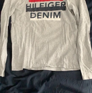 Tommy Hilfiger Denim lång ärmar tröja - Detta är en fin fin lång ärmad tröja som är tunn och perfekt när det är för varmt för hoodie men för kallt för t-shorts. Den har fina detaljer med blå, rött och vitt på det gråa som man kan se på bild 2.