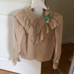 Stockholmsstil Gina Tricot Ny Beige Blus  - Beige blus med fina volanger från Gina Tricot, helt oanvänd Originalpris: 429. Storlek: 34 / XS-S. RABATTERAD PRIS NU ENDAST 135 KR