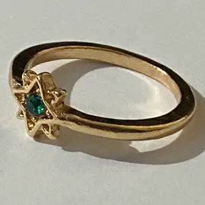 Silverring med gulddetaljer i form av en grön kristall stjärna.
