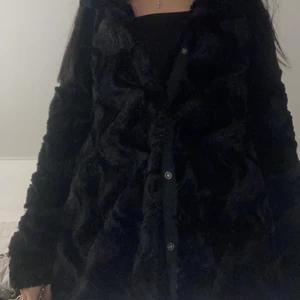 Svart päls kappa  - En svart pälskappa med knappar. Kappan går över rumpan och är i storleken xs men passar definitivt en S också. Kappan är använd ca 3 gånger 
