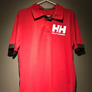 Röd Helly Hansen piké  - Säljer röd Helly Hansen Piké, aldrig använd.