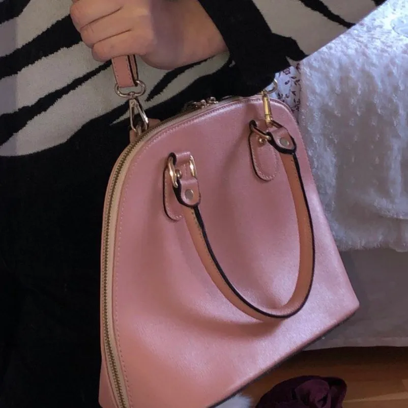 Rosa väska 💕 väskbandet går enkelt att ta av (se bild 2). Köpt i Italien för 2 år sedan men har inte använts mycket. Den har flera fack inuti. Ena handtaget på dragkedjan har lossnat, men går säkert att fixa om man vill (se bild 3)👍🏼. Väskor.