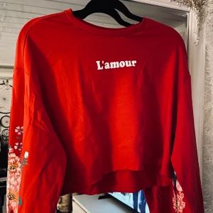 Croppad sweatshirt ❤️ - Väldigt sparsamt använd croppad sweatshirt med texten ”L’amour” ❤️ Den har vackra blommor längs ärmarna och är i storlek M ❄️ Skriv privat om du har frågor!