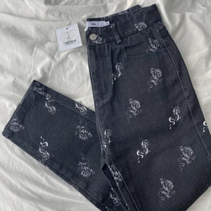 Helt nya jeans - Helt nya raka svarta/mörkgråa jeans med drakar på från Adika🤍 jeansen är köpta i newyork för ca 2 år sedan men aldrig kommit till användning då de är försmå för mig. De är köpta för 52$. Skicka privat vid frågor, intresse eller för exakta mått🤍