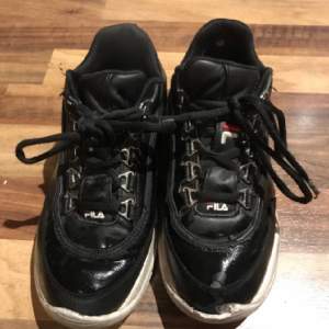  Välanvända svarta fila skor, skon har tappat en liten del längst fram på skon, lite sprickor här och där. Storlek 37