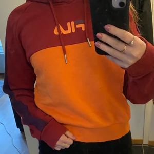 FILA hoodie i storlek M - En superfin hoodie från FILA. Tröjan är sparsamt använd och därför i fint skick. Färgerna är mörkröd och orange, samt en mörklila detalj på armarna. Priset är 120kr eller bud (frakt tillkommer om inte köparen kan hämta plagget). Betalning sker via swish!