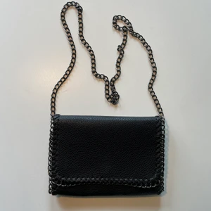 Stella McCartney-liknande väska - En svart crossbody-väska i skinnimitation. Detaljer i kedja och med kedjeband. Ett stort fack med två små inuti, varav det ena har en dragkedja. Liknar handväskan från Stella McCartney.