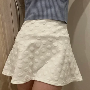 Vit minikjol - Fin minikjol med prickig struktur. Säljer därför att den är för liten, använd få gånger. Dragkedja i midjan på ryggen. Kjolen är a-linje formad. Kjolen är storlek XXS men skulle kunna fungera som XS. Passar både sommar och vinter eftersom den är i ett lite tjockare material.
