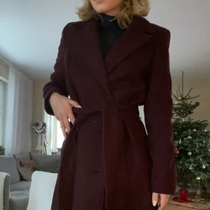 Mango kappa - Säljer denna superfina kappan från Mango i storlek L! Den är i väldigt bra skick och är knappt använd. Den har knappar som man knäppa med och en jättefin knytning som man antingen kan ha fram eller bak. Färgen är vinröd.