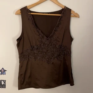 Topp/Linne brun med spets/mönster i  - Ett brunt linne/topp i silke med V-ringning med mönster kring V-ringningen och ner. Användes under 2000-talet och väl bevarad. 